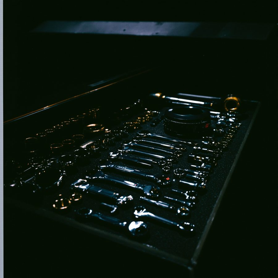An open tool drawer under a low light: combination wrenches, sockets and a ratchet laid into cut foam.