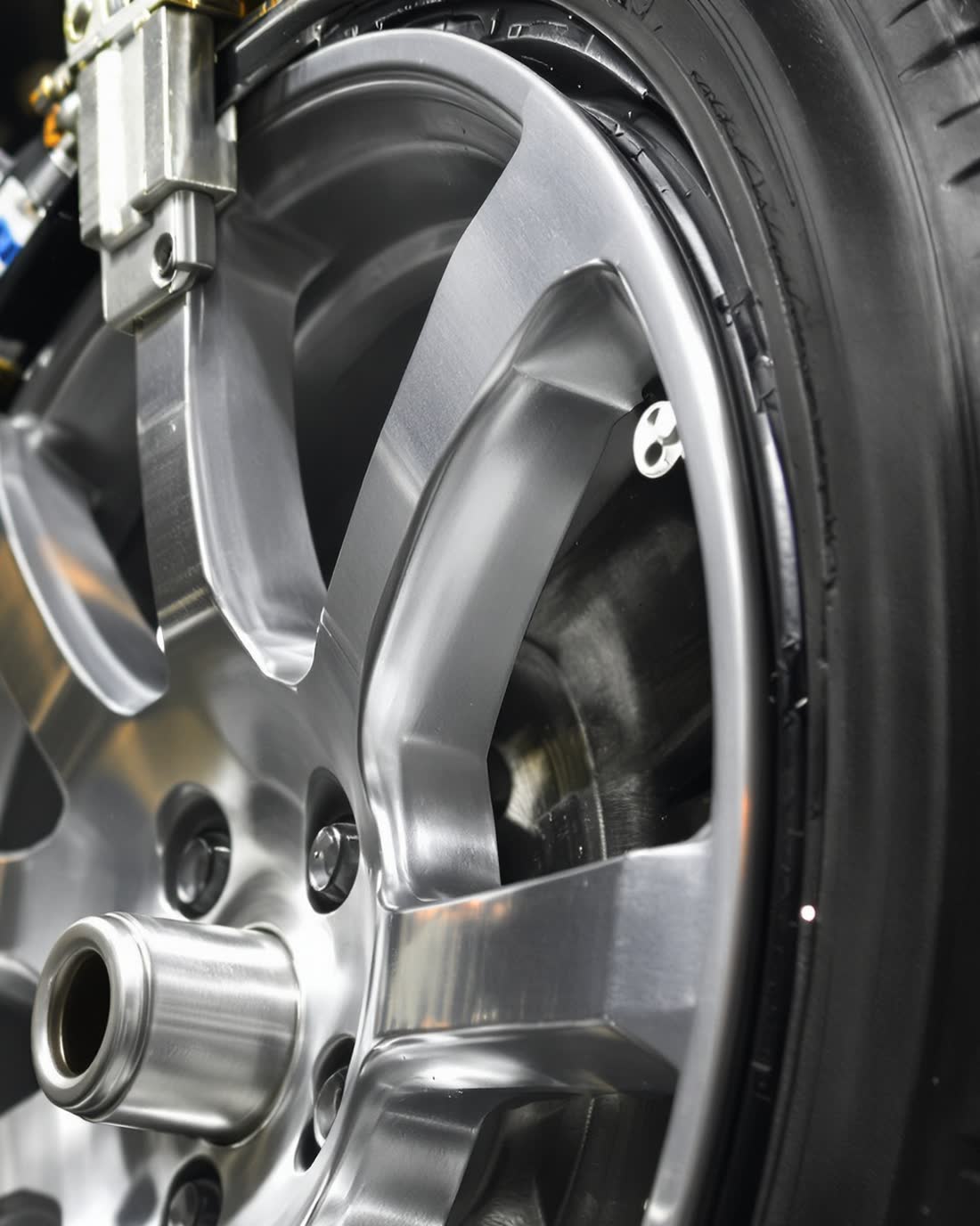 A tire and alloy wheel on a balancing machine, a technician's hand steadying the rim.